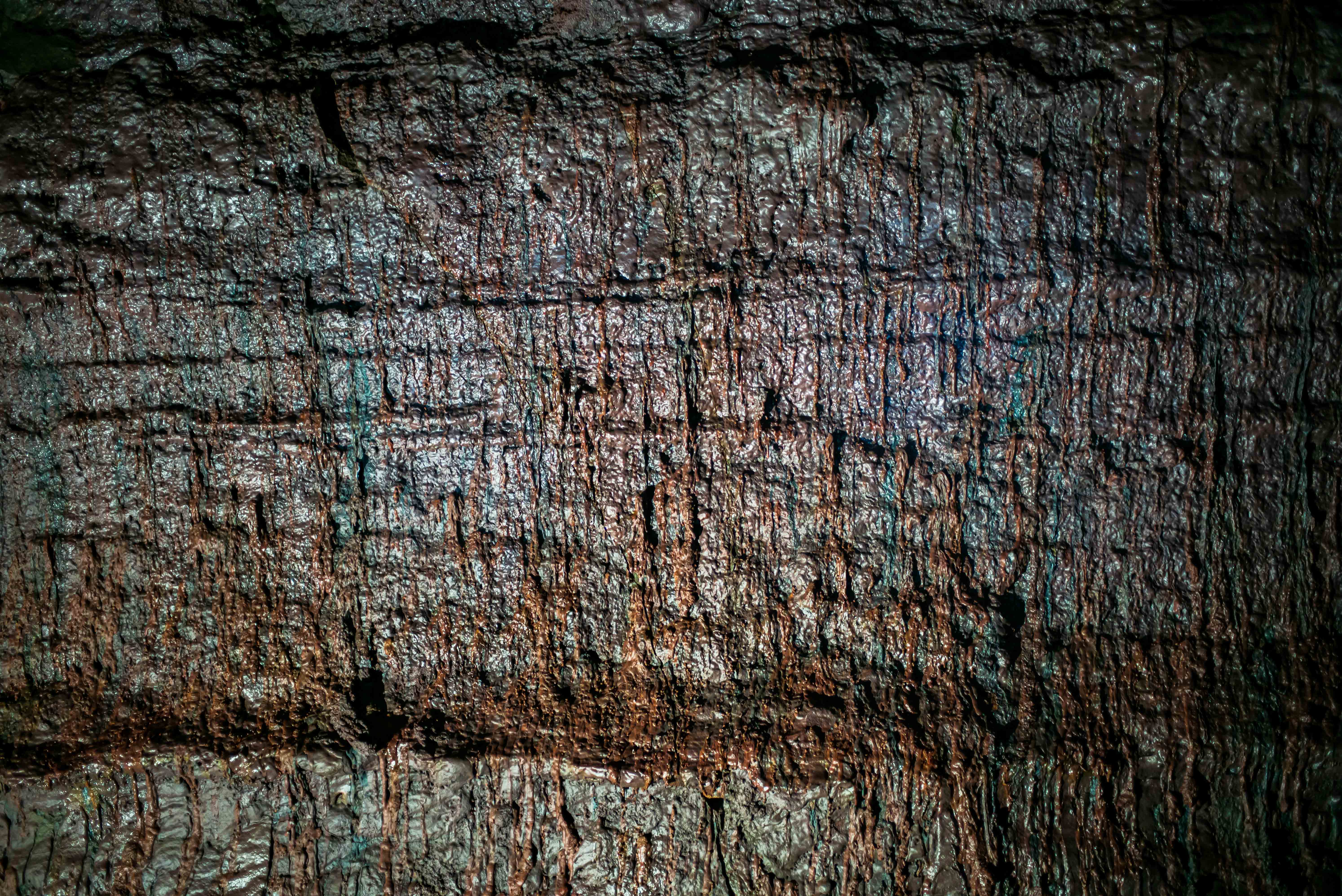Close view of a dark lava-cave wall at Víðgelmir, showing horizontal bands and fine vertical textures in the cooled volcanic rock.