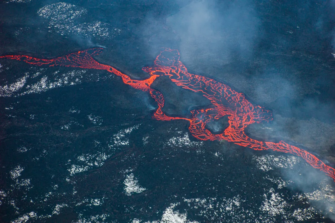 AAerial view of glowing red-orange lava branching through a dark crusted lava field during the Holuhraun eruption in Iceland.